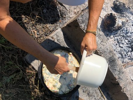 Pfannenkuchenteig wird in eine große Pfanne gegossen, umgeben von Steinen und Gras.