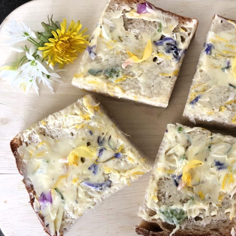 Brot mit bunten essbaren Blüten und Kräutern auf einem Holzbrett.